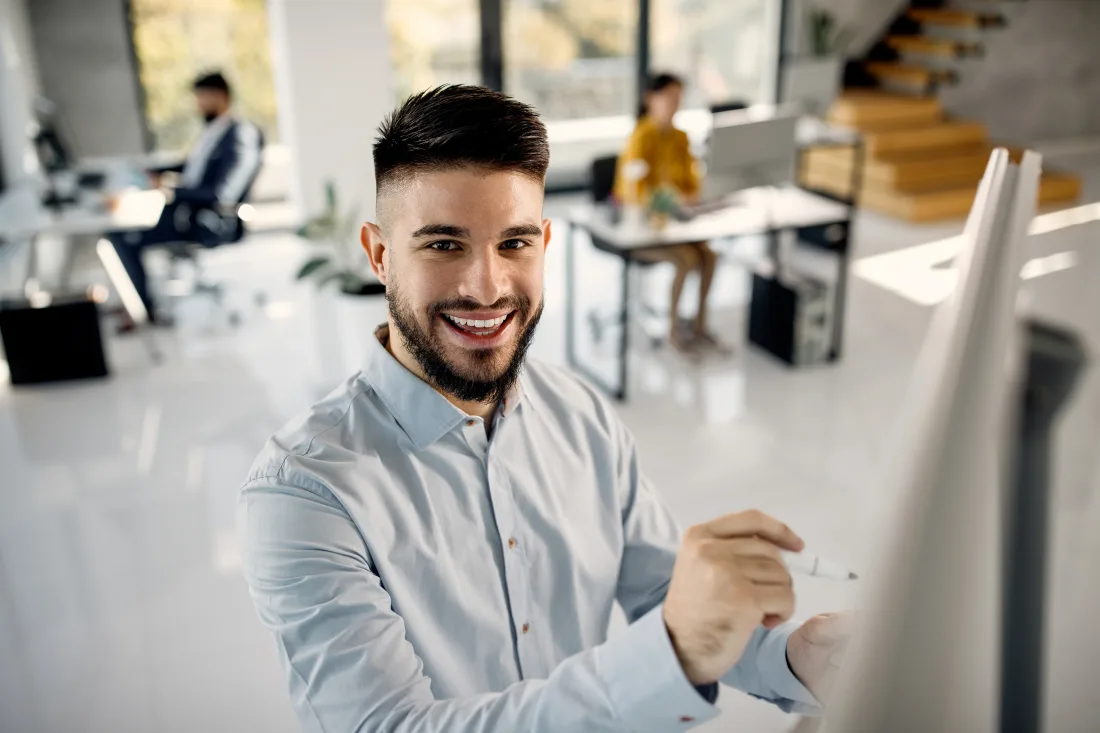 Empresario sonriente exponiendo ideas en una pizarra dentro de una oficina moderna