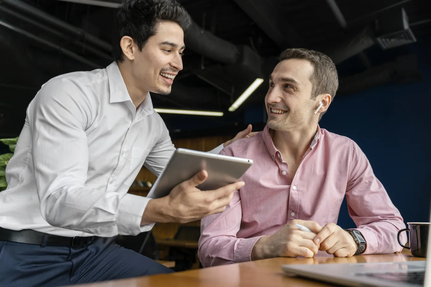 Dos profesionales conversando y revisando información en una tableta dentro de una oficina